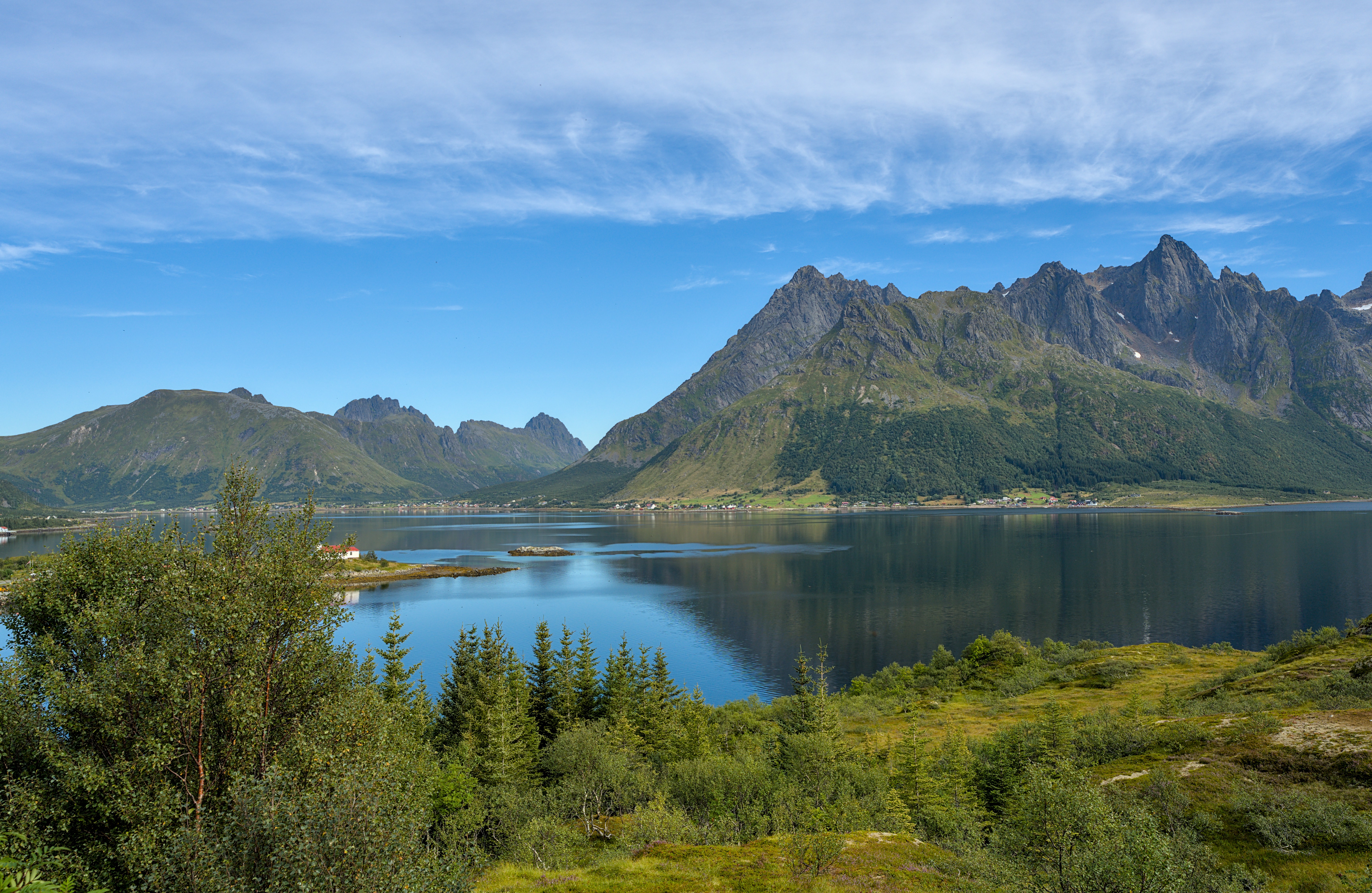 Beeindruckende Aussicht auf die Lofoten in Norwegen mit Bergen, klarem Himmel und einem ruhigen See im Vordergrund.
